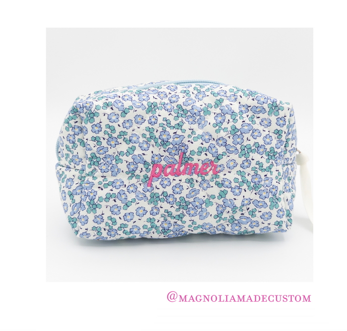 A rectangular cosmetic pouch with a white background and a blue and green floral pattern, featuring the name 'palmier' embroidered in pink across the front. The pouch is shown on a light gray background with a social media handle watermark at the bottom.