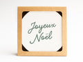 The Joyeux Noël Coaster Set by Onderkast Studio comes in a square brown recyclable box with a white card reading “Joyeux Noël” in green script, making it the perfect gift for letterpress coaster lovers or holiday treasures.