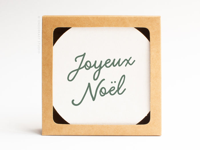 The Joyeux Noël Coaster Set by Onderkast Studio comes in a square brown recyclable box with a white card reading “Joyeux Noël” in green script, making it the perfect gift for letterpress coaster lovers or holiday treasures.