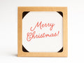 The Merry Christmas Coaster Set by Onderkast Studio comes in a brown, hand-assembled recyclable kraft box with a white card inside that says “Merry Christmas!” in red cursive letters.