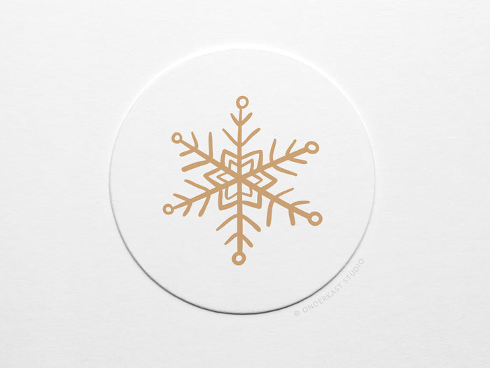 The Snowflake Coaster Set by Onderkast Studio features a gold geometric snowflake on a white circle, offering a minimalist and elegant winter design—ideal for handmade letterpress coasters made from durable pulp board.